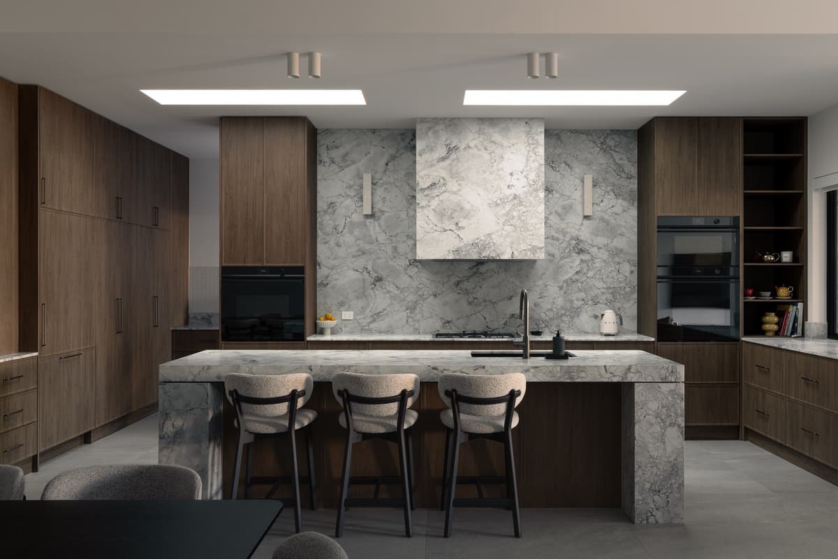 Dark kitchen at Cuthbert: walnut-toned joinery and a dolomite marble island, splashback and rangehood